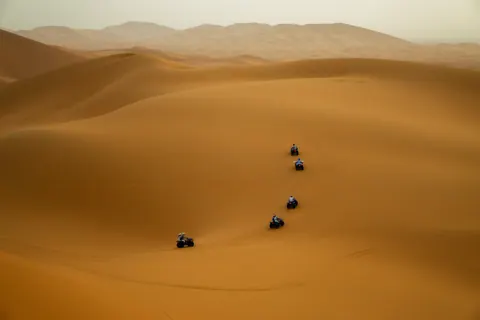 Small figures crossing broad Sahara dunes in Morocco